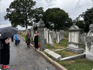 people are standing in the rain in a cemetery, one person is holding a line of thread